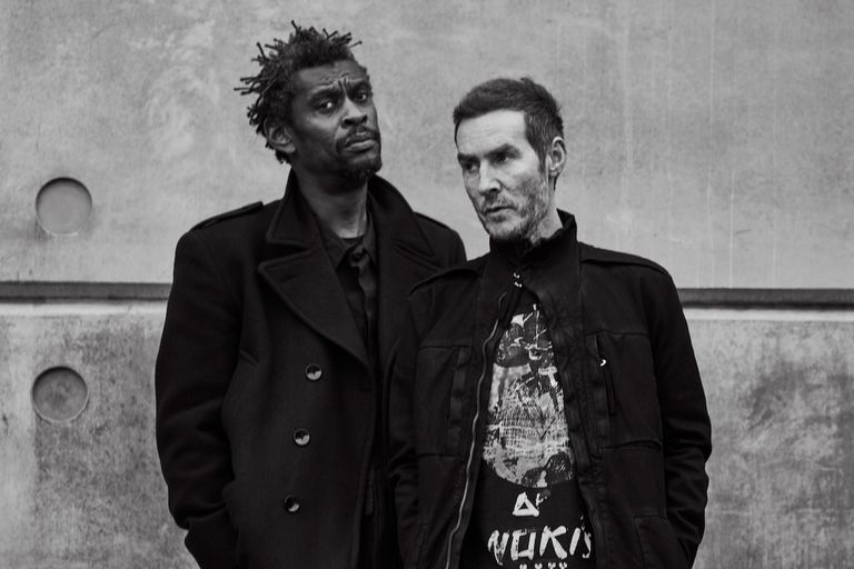 Black and white portrait of trip-hop band Massive Attack members Robert Del Naja and Grant Marshall posing together against an industrial wall